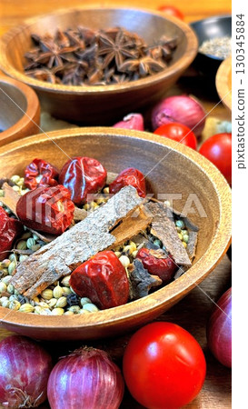 Wooden vessels filled with colorful spices, dried chilies, star anise, cinnamon bark surrounding fresh red tomatoes and purple onions, presenting rich culinary palette Wooden vessels filled with colorful spices, dried chilies, star anise, cinnamon bark surrounding fresh red tomatoes and purple onions, presenting rich culinary palette 130345884