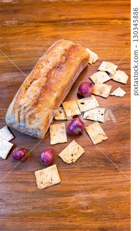 Rustic wooden surface displaying golden brown bread, crisp crackers, and pearl like onions in artful, appetizing arrangement 130345886