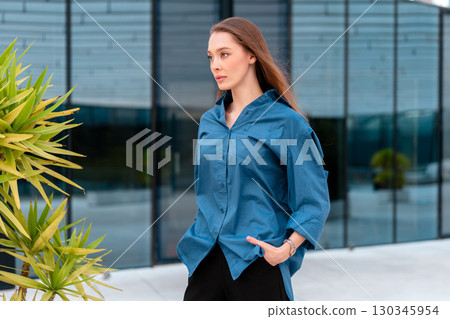Confident woman in blue shirt walking outdoors 130345954