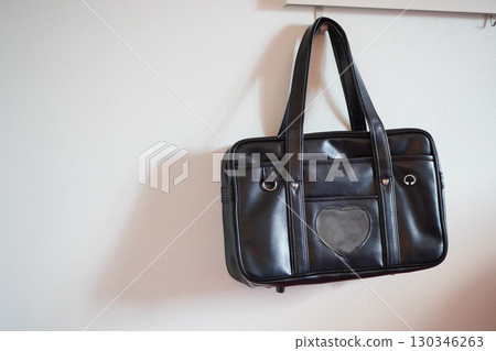 A black school bag hanging on the wall. A student bag. A standard school bag used for commuting to school. 130346263