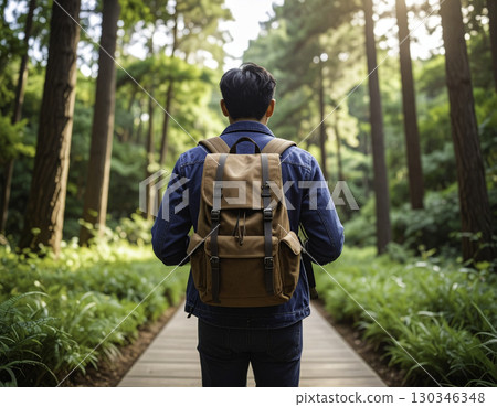 Rear view of a man wearing a backpack walking along a forest trail 130346348