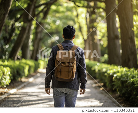 一名男子背著背包沿著森林小徑行走的後方視圖 130346351