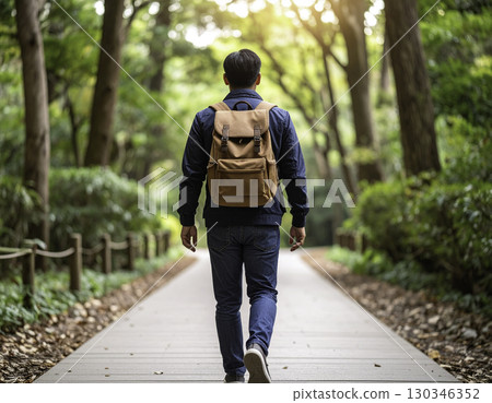 一名男子背著背包沿著森林小徑行走的後方視圖 130346352