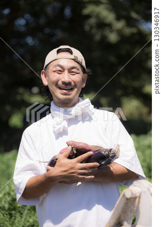 一名男子在田裡收割蔬菜。圖片為農民或農業工人。特寫鏡頭：一名男子麵帶微笑，正看著鏡頭 130346917