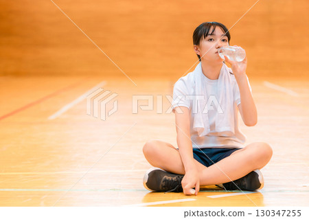 小學、國中和高中的女生穿著運動服在體育館喝瓶裝水補充水分 130347255
