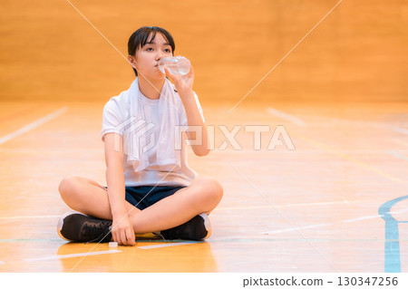 小學、國中和高中的女生穿著運動服在體育館喝瓶裝水補充水分 小學、國中和高中的女生穿著運動服在體育館喝瓶裝水補充水分 130347256