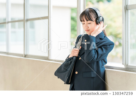 小學、國中、高中女生穿著校服在學校走廊上戴著耳機聽音樂 小學、國中、高中女生穿著校服在學校走廊上戴著耳機聽音樂 130347259