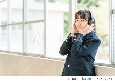 Elementary school, junior high school, and high school girls in uniforms listening to music with headphones in the school corridor 130347263