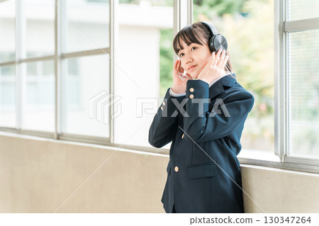 Elementary school, junior high school, and high school girls in uniforms listening to music with headphones in the school corridor Elementary school, junior high school, and high school girls in uniforms listening to music with headphones in the school corridor 130347264