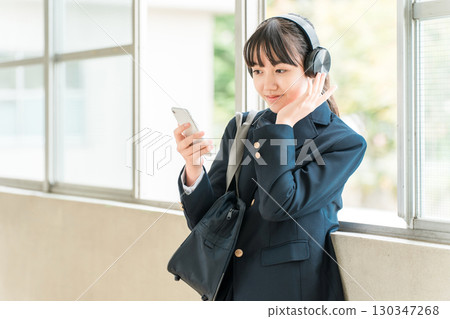 小學、國中、高中女生穿著校服在學校走廊上戴著耳機聽音樂 130347268