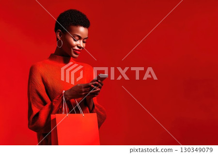 Beautiful smiling African woman with short hair holding shopping bag and using smartphone for online shopping. Sale and discount season concept, banner with fashionable woman and copy space Beautiful smiling African woman with short hair holding shopping bag and using smartphone for online shopping. Sale and discount season concept, banner with fashionable woman and copy space 130349079