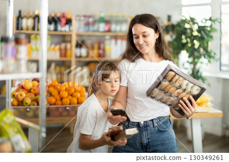 Girl with mother customers at shop scans QR code on sweets package using phone camera Girl with mother customers at shop scans QR code on sweets package using phone camera 130349261