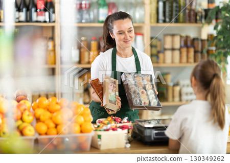 Female seller offers to buy cookies to teenage girl in interior of grocery supermarket Female seller offers to buy cookies to teenage girl in interior of grocery supermarket 130349262