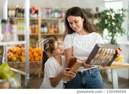 Mother consults with her daughter about which sweets to buy in the grocery section of supermarket - nougat or cookies Mother consults with her daughter about which sweets to buy in the grocery section of supermarket - nougat or cookies 130349269
