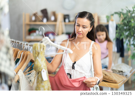 Near rack, woman buys summer dress, chooses items. Near rack, woman buys summer dress, chooses items. 130349325