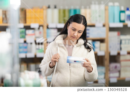 Middle-aged woman customer choosing ointment in box in drugstore Middle-aged woman customer choosing ointment in box in drugstore 130349328
