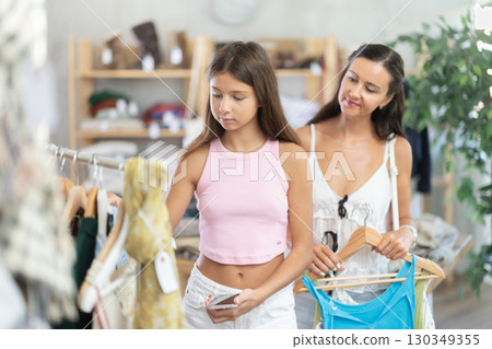 Near rack, daughter with mom buys something summer cloth, chooses items. 130349355