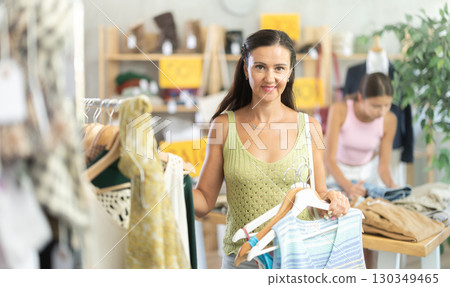 Happy middle-aged woman choosing something for summer in clothing store 130349465