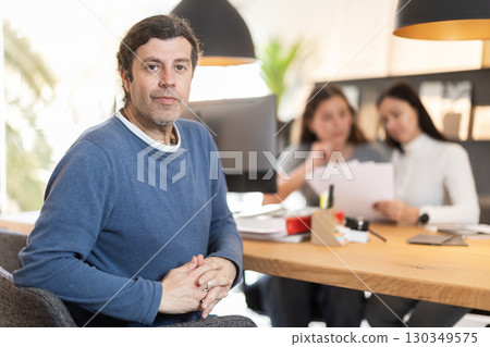 manager of a European furniture salon sits at a table against the background of customers 130349575
