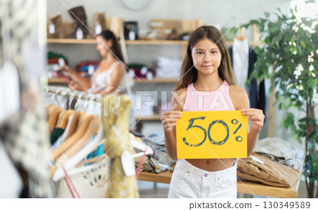Teen girl with poster in hands announce mega 50percent discounts in womens clothing store Teen girl with poster in hands announce mega 50percent discounts in womens clothing store 130349589