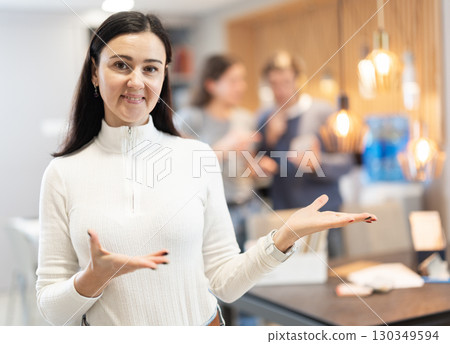 Female salesperson invites to choose modern furniture in furniture store 130349594