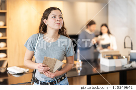 Female buyer with samples of material chooses kitchen set in furniture store 130349641