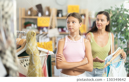 Stubborn teen girl is moody and shows dissatisfaction while shopping in cloth store with her mother Stubborn teen girl is moody and shows dissatisfaction while shopping in cloth store with her mother 130349642
