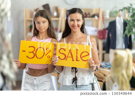 Teen girl and mom holds yellow poster informing about discounts in store 130349644