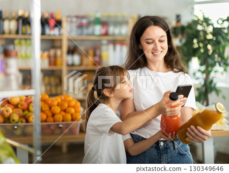 Mother and daughter choose bottles of juice and scan QR code with smartphone in supermarket 130349646