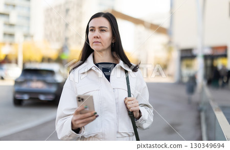 Elegant woman with smartphone walking on street of european city Elegant woman with smartphone walking on street of european city 130349694