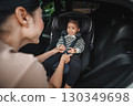 mother is fastening safety belt to happy toddler girl in car seat, safety baby chair travelling 130349698
