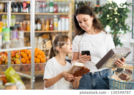 Daughter and mother choose delicious cookies in supermarket - scan QR code on label with smartphone Daughter and mother choose delicious cookies in supermarket - scan QR code on label with smartphone 130349787
