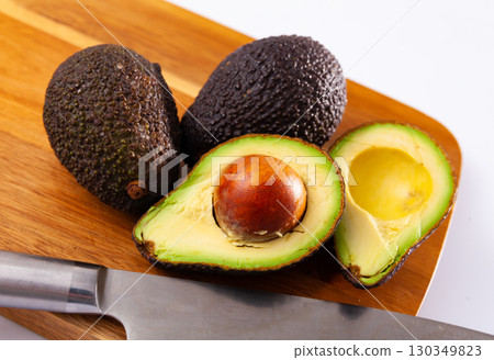 Whole and halved avocados on wooden cutting board on white Whole and halved avocados on wooden cutting board on white 130349823