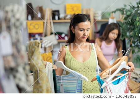 Near rack, woman buys something summer cloth, chooses items. 130349852