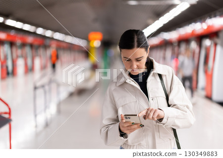 Female passenger with mobile phone in his hands awaits at station arrival of metro train Female passenger with mobile phone in his hands awaits at station arrival of metro train 130349883