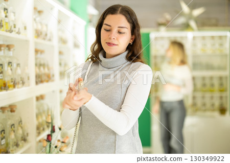 Girl sniffs fragrance of perfume, chooses scent spray, woman shopping in background 130349922