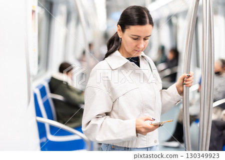 Woman stand in metro carriage, scrolls through social media feed 130349923
