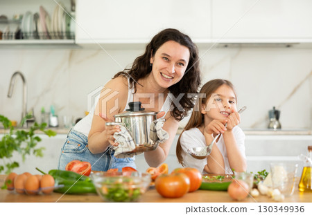 Mom and little daughter are standing at kitchen table with dishes in their hands. Mom and little daughter are standing at kitchen table with dishes in their hands. 130349936