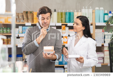 Man chooses pills in modern pharmacy. Female pharmacist helps with choosing medicine 130349969