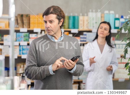 Male customer looking for something in drugstore. Female pharmacist offers him medicines 130349987