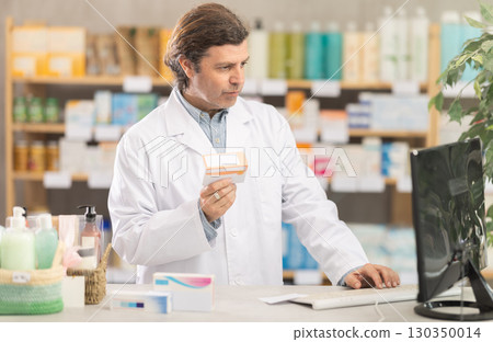 Male pharmacist looking for pills on computer Male pharmacist looking for pills on computer 130350014