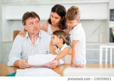 Upset adult man reviewing documents at table with family Upset adult man reviewing documents at table with family 130350021