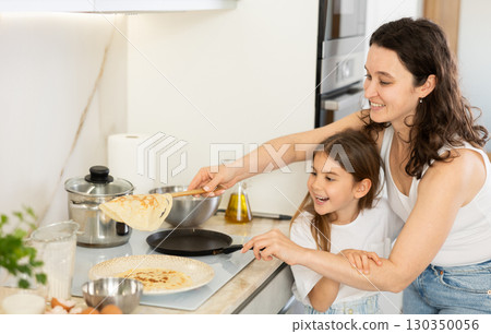 Happy mother and daughter frying pancakes in the kitchen Happy mother and daughter frying pancakes in the kitchen 130350056