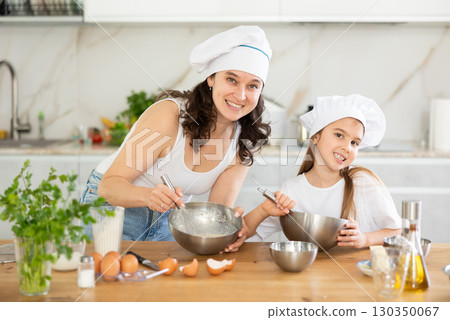 Happy mother and her daughter whisking ingredients in metal bowl in the kitchen 130350067
