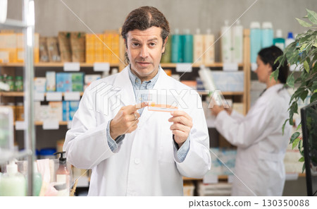 Friendly male pharmacist standing at drugstore with medical product in hands 130350088