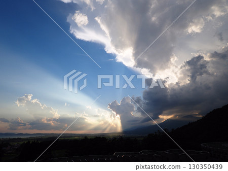 On a summer evening, the sun hides behind cumulonimbus clouds, creating a radiant light that is both dramatic and beautiful. 130350439