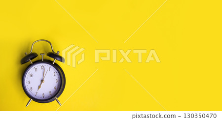 Black alarm clock showing seven oclock on yellow background with copy space. Black alarm clock showing seven oclock on yellow background with copy space. 130350470