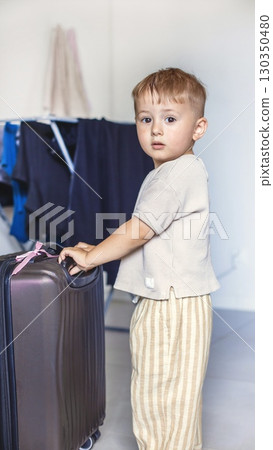 Child standing in the middle of a room with a large black suitcase, symbolizing travel, family journey, or adventure. Child standing in the middle of a room with a large black suitcase, symbolizing travel, family journey, or adventure. 130350480