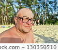 Portrait of a smiling middle-aged man in glasses relaxing on a beach by the river, enjoying summer 130350510