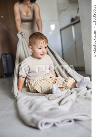 Happy child spending time at home while mother playfully pulls him on a blanket across the floor 130350515
